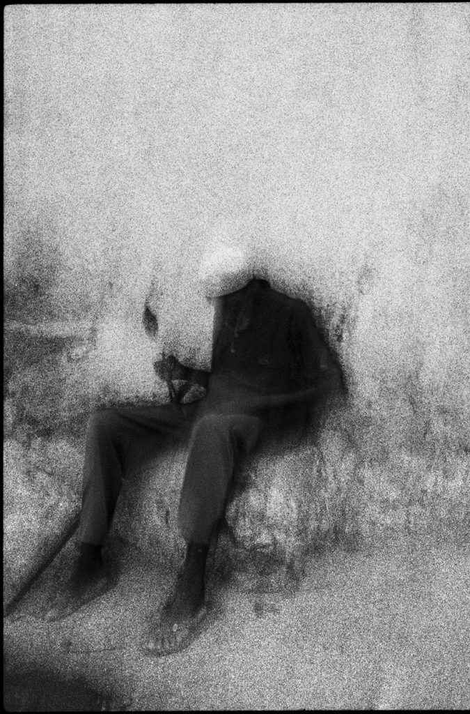 Photographie argentique en noir et blanc d'un homme assis, adossé à un mur et tenant une chandelle dans une rue du Mercato à Addis Abeba/Ethiopie.