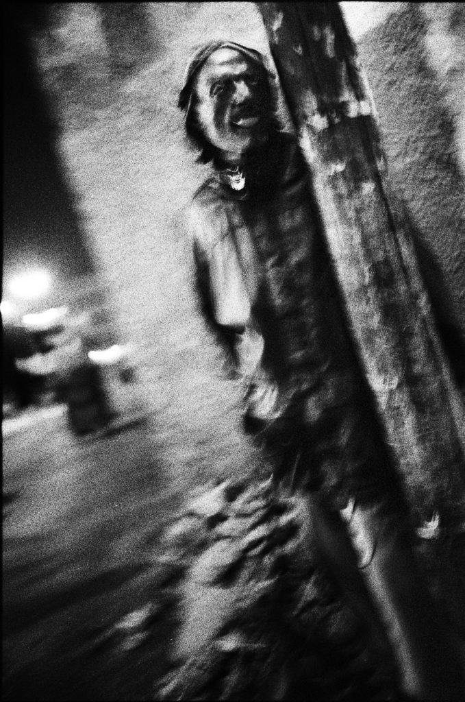 Photographie argentique en noir et blanc d'un homme se tenant debout contre un poteau, la nuit à Jimma/Ethiopie.