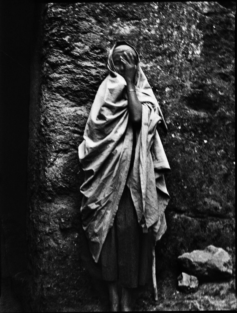 Photographie argentique en noir et blanc d'une femme en prière adossée au mur d'une église à Lalibela/Ethiopie.