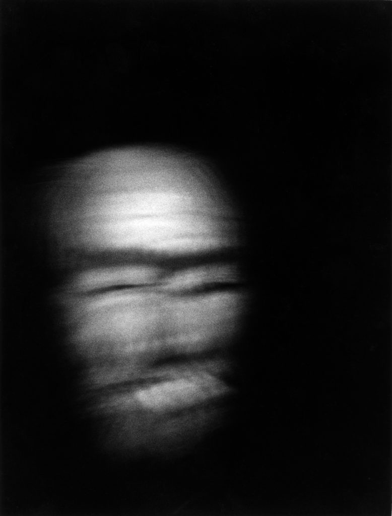 Photographie argentique en noir et blanc d'une tête d'homme, cigarette en bouche, une nuit dans Paris.