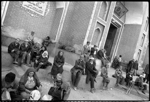 Photographie argentique en noir et blanc de femmes et d'hommes ouïgours assis devant l'entrée d'une mosquée à Kashgar/Chine.