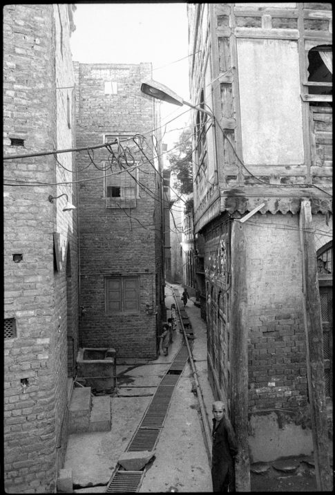 Photographie argentique en noir et blanc d'un garçon se tenant debout, adossé au mur d'une ruelle de Peshawar/Pakistan.