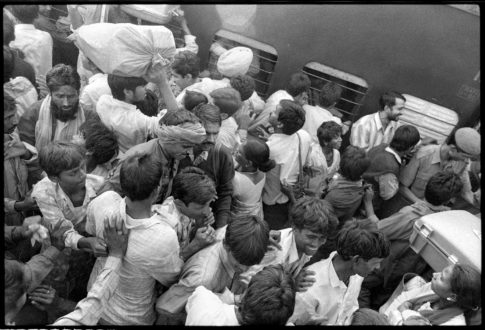 Photographie argentique en noir et blanc d'une foule de voyageurs acculés les uns contre les autres sur un quai de gare à Delhi en Inde.