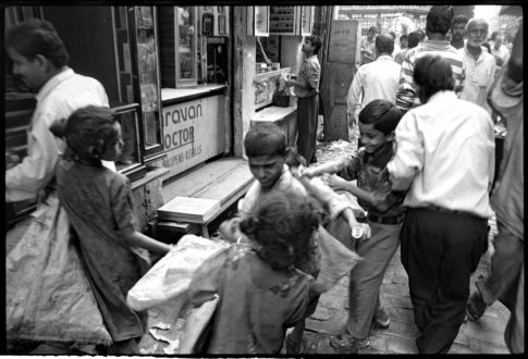 Photographie argentique en noir et blanc d'enfants et d'adultes en marche se bousculant dans une petite rue de Calcutta en Inde.