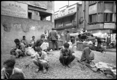 Photographie argentique en noir et blanc de travailleurs se tenant assi autour d'une tchaï shop (stand où est préparé et consommé du thé) dans un quartier populaire de Calcutta/Inde.