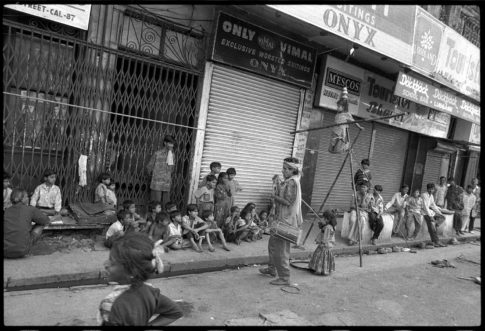 Photographie argentique en noir et blanc d'une famille de funambule sur un trottoir de Calcutta/Inde donnant une représentation devant des enfants de la rue.