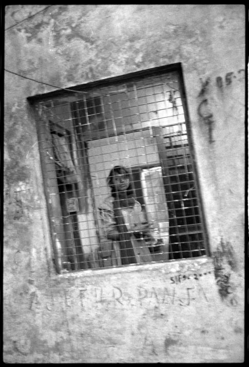 Photographie argentique en noir et blanc d'une jeune femme derrière une fenêtre grillagée dans Calcutta/Inde.